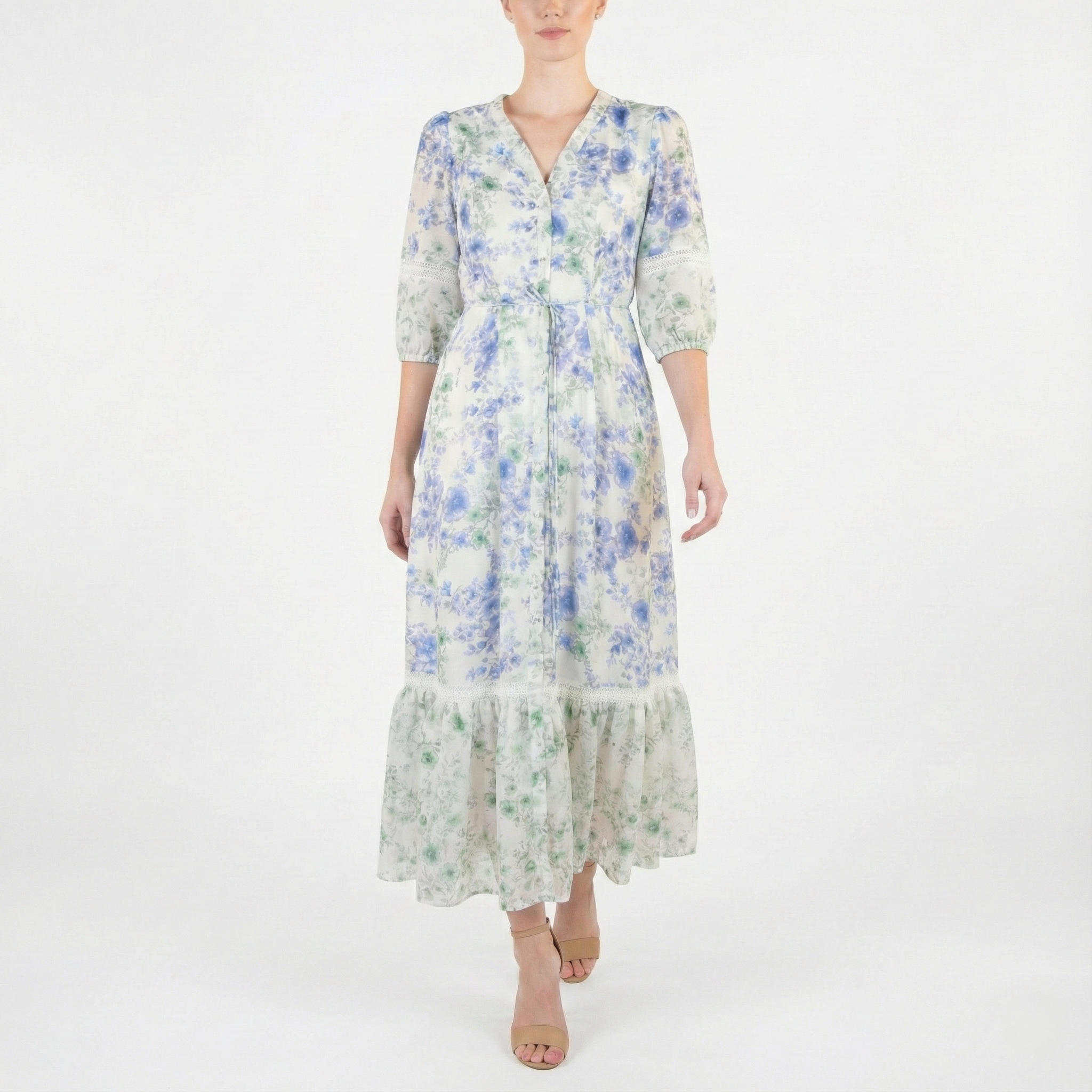Model wearing a light ivory midi dress with blue and green floral print, V-neckline, three-quarter sleeves, tie waist, and ruffled hem, styled with nude heels.
