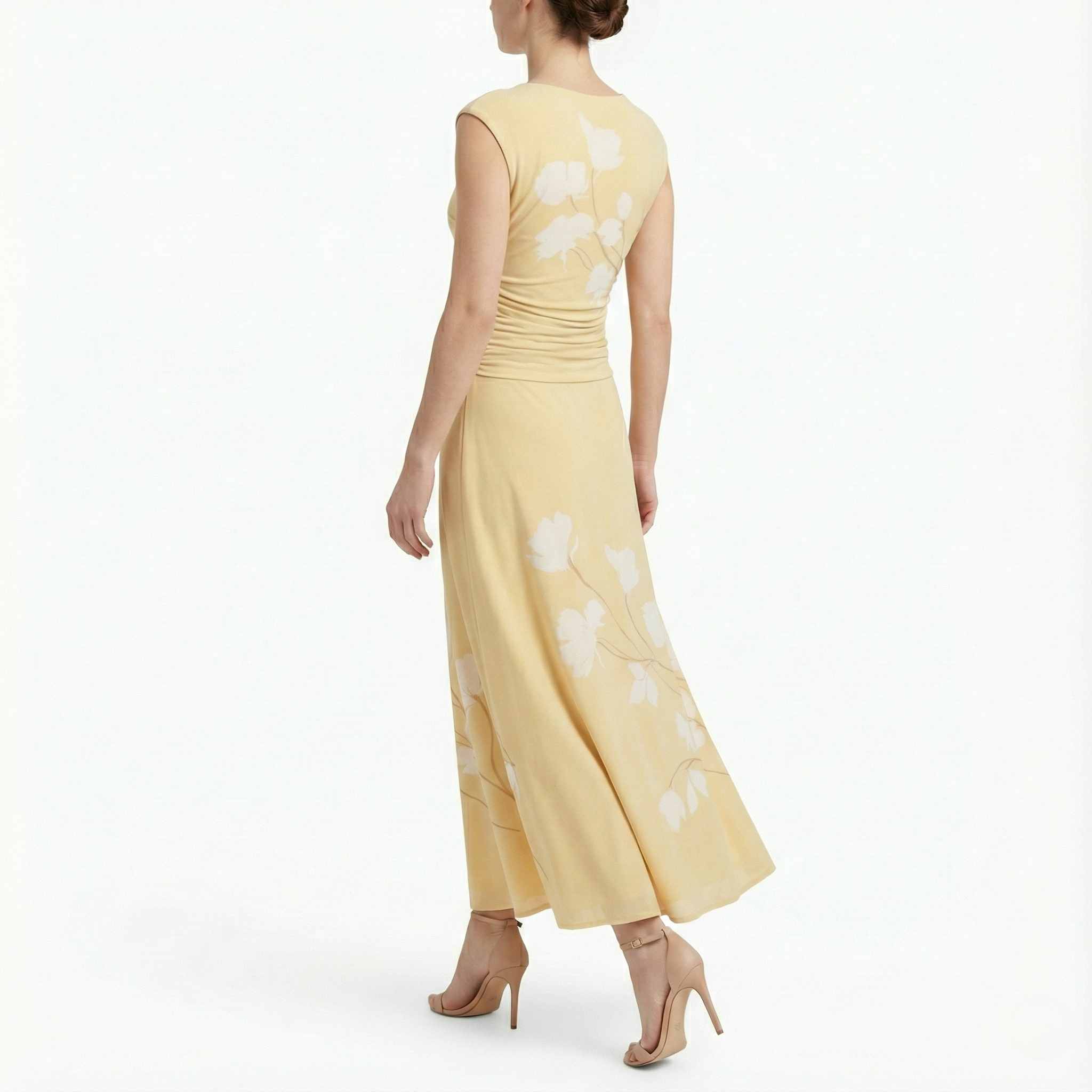 Back view of cornsilk yellow sleeveless midi dress with white floral print, softly ruched waist, flowing skirt, and nude high-heel sandals.
