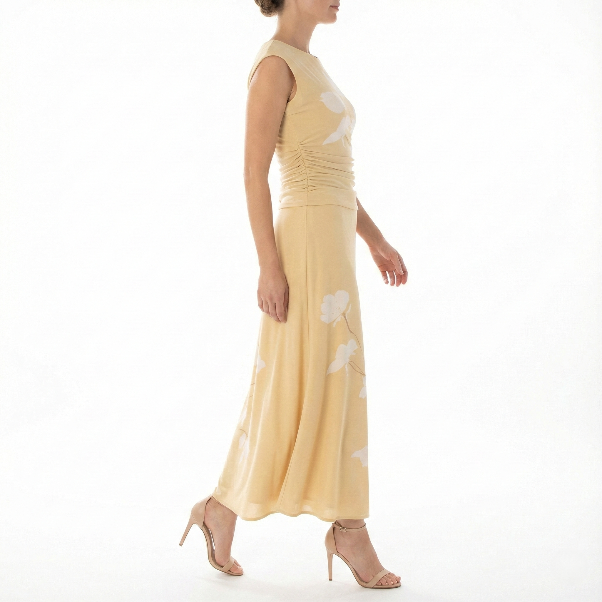 Side profile of model wearing a cornsilk yellow sleeveless midi dress with white floral print, ruched bodice, flowy midi skirt, and nude high-heel sandals.