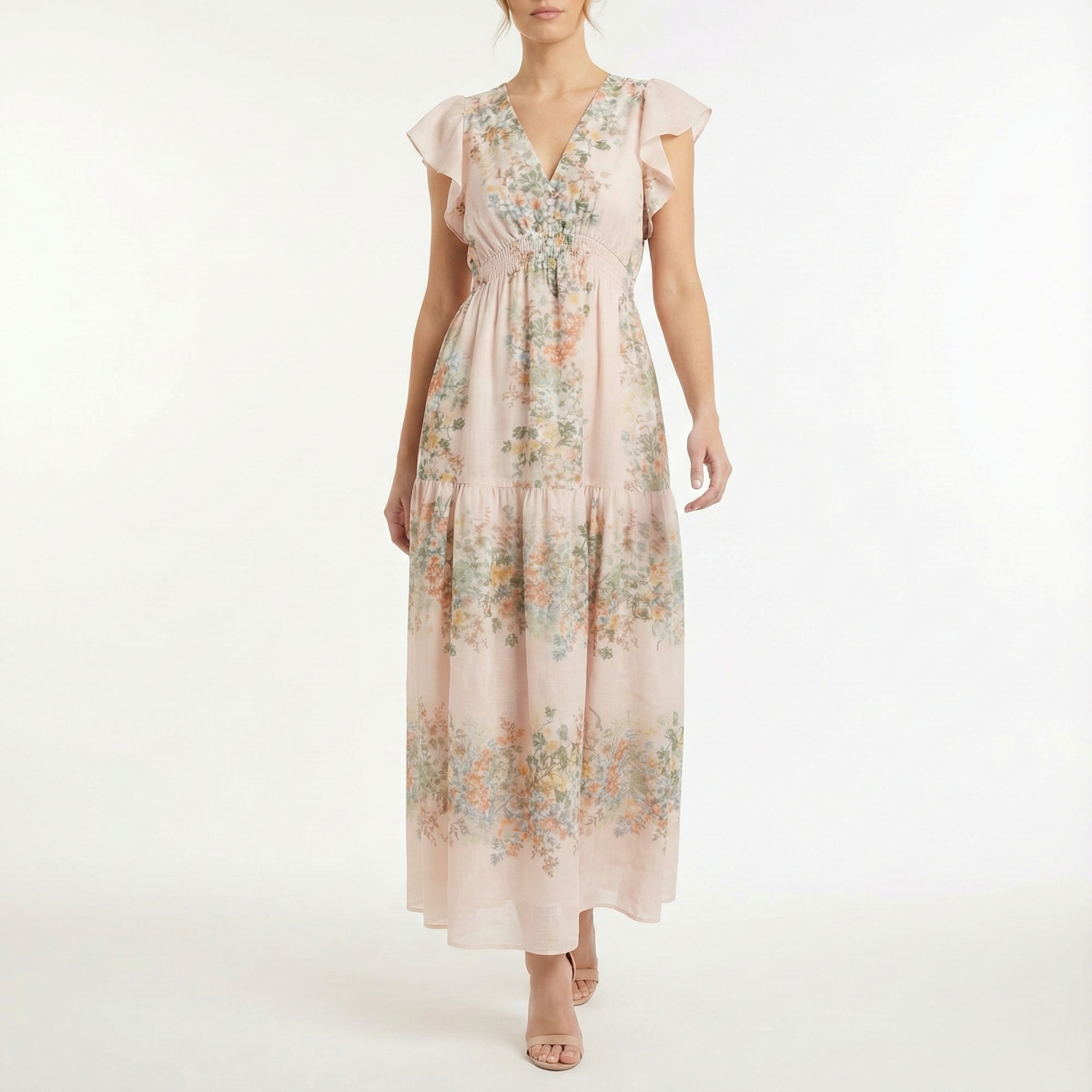Blush pink floral chiffon maxi dress with flutter sleeves, V-neckline, smocked waist, and tiered skirt, shown from the front on a model wearing nude heels.