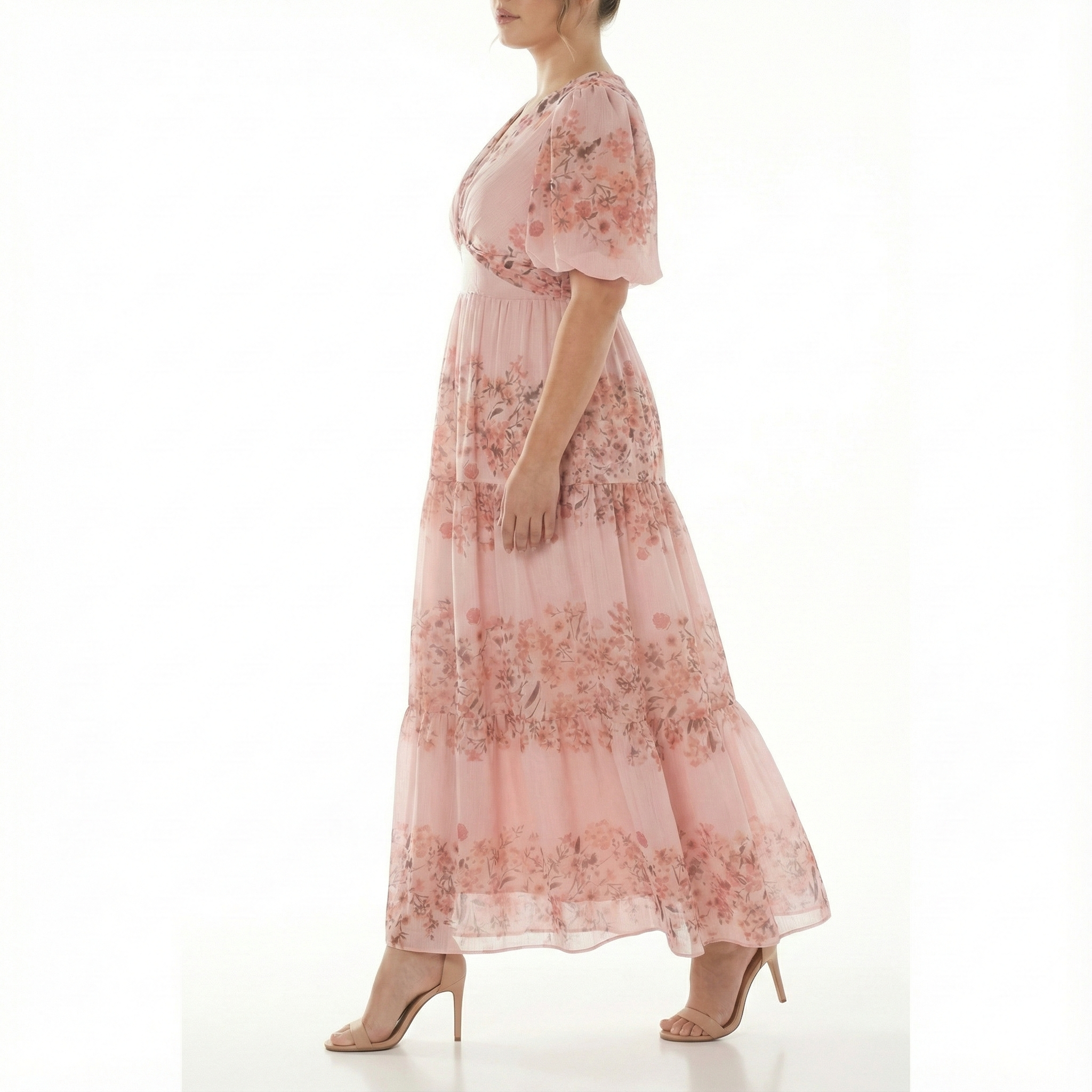 Side view of model walking in blush pink floral chiffon maxi dress featuring short puff sleeves, V-neck bodice, fitted waist, and airy tiered skirt.
