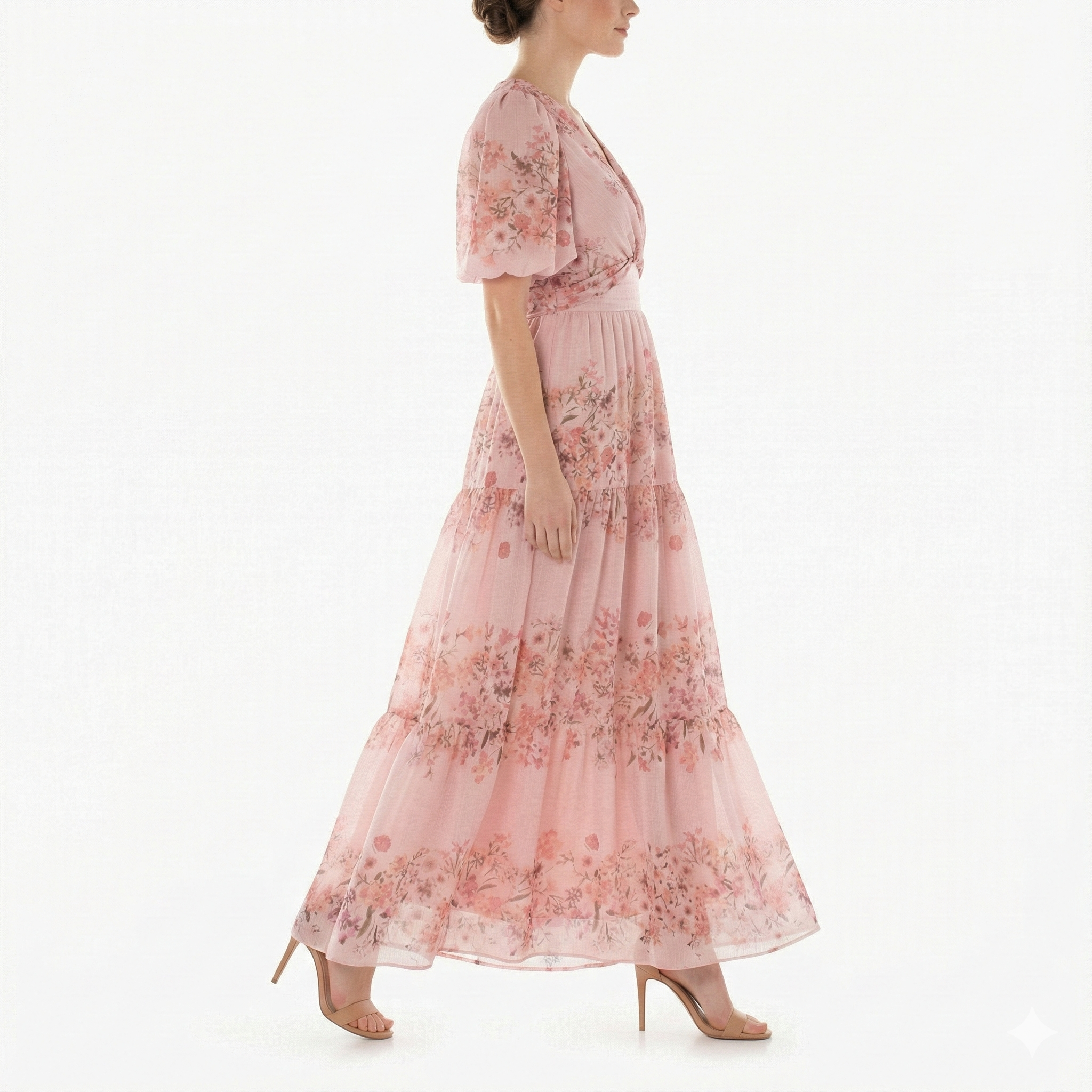 Side profile of model walking in blush pink floral chiffon maxi dress with puff sleeves, V-neck bodice, fitted waist, and flowing tiered skirt.