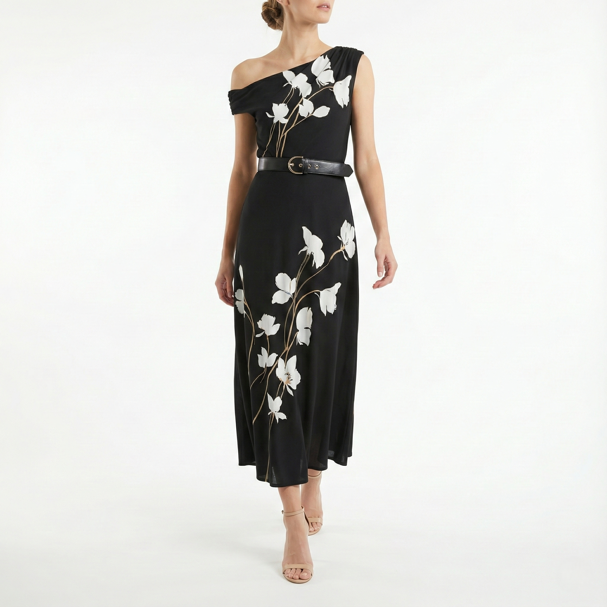Model wearing a black one-shoulder midi dress with white floral print and waist belt, shown from the front, styled with nude high-heel sandals.
