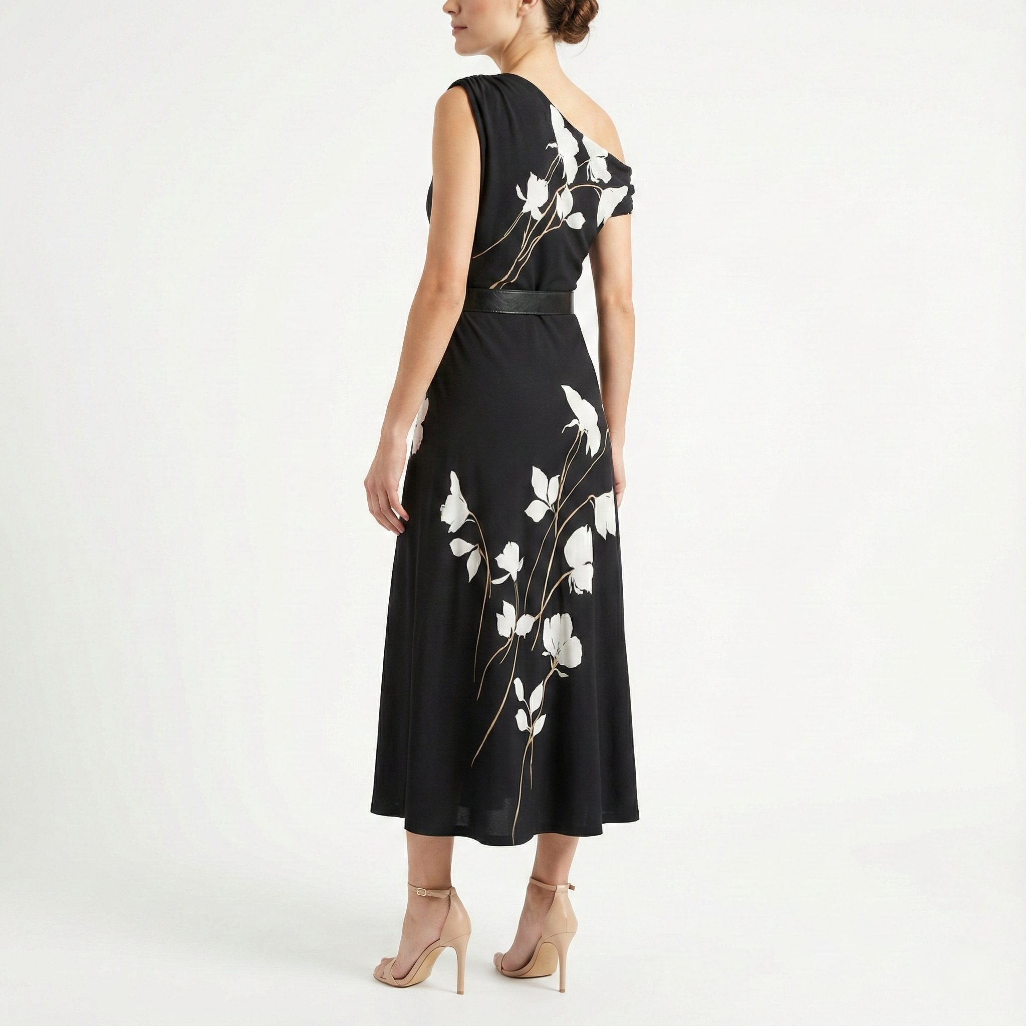 Back view of black one-shoulder midi dress with white floral pattern and belted waist, paired with nude high-heel sandals.