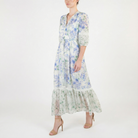 Side view of a light ivory floral midi dress with blue and green flowers, V-neck, sheer three-quarter sleeves, tie waist, and flowing ruffled hem.