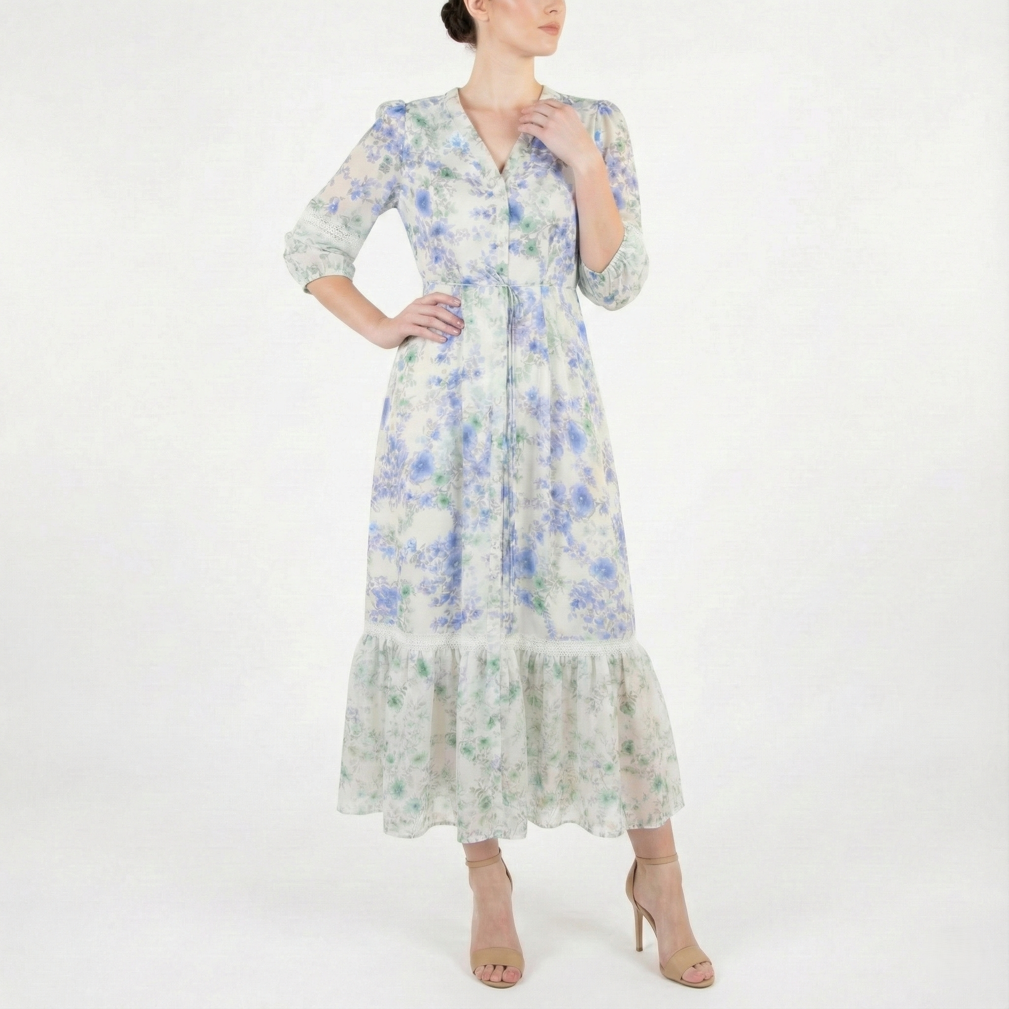 Model posing in a light ivory blue-and-green floral midi dress with V-neckline, tie waist, airy sheer sleeves, and soft ruffle hem.