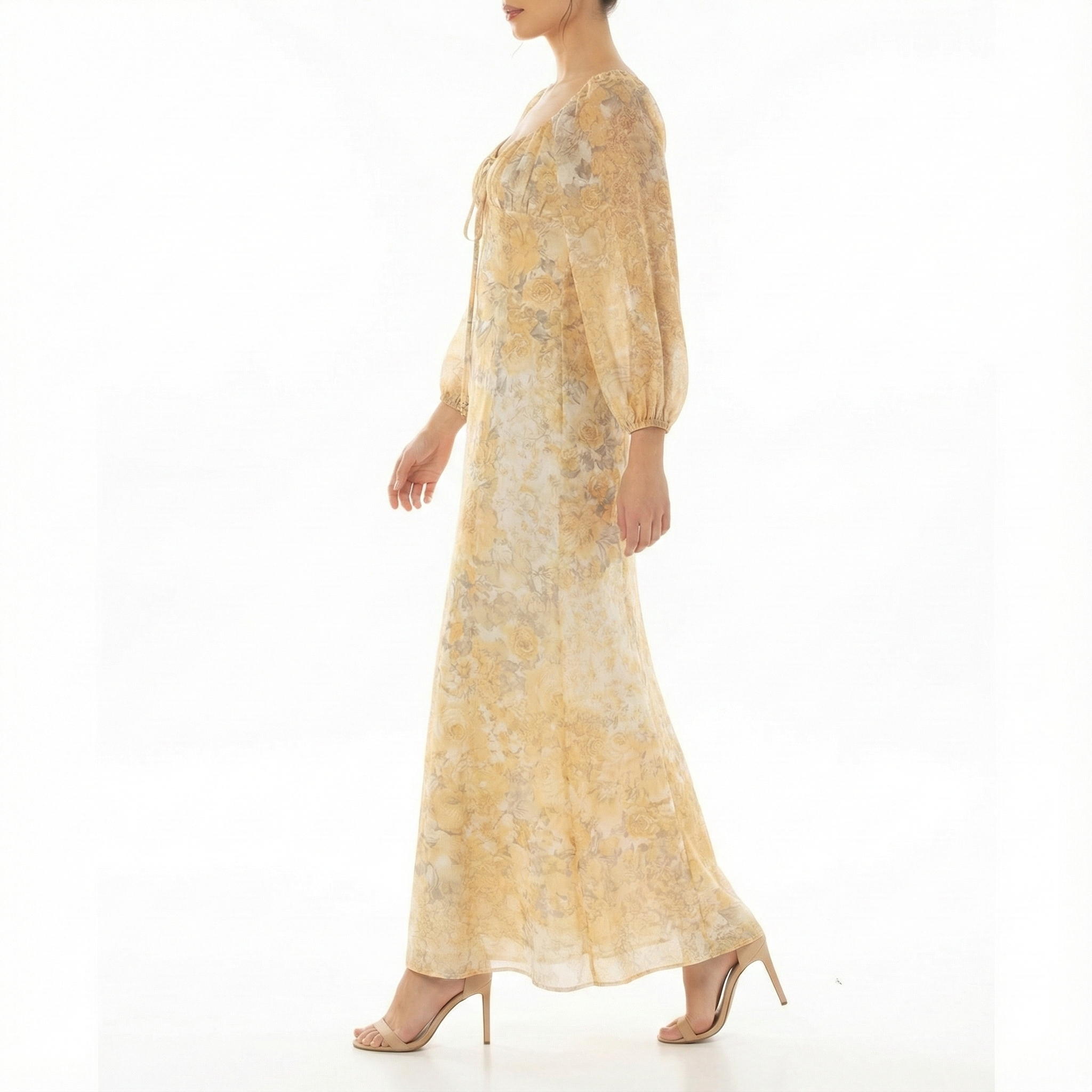 Side view of a women’s yellow floral maxi dress with long sheer puff sleeves, scoop neckline, and flowing chiffon skirt, styled with nude high-heel sandals.