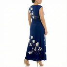 Three-quarter back view of a women’s navy blue sleeveless maxi dress with ivory floral print, featuring a fitted bodice, ruched waist, and elegant floor-length design.