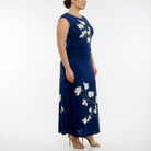 Side view of a women’s navy blue sleeveless maxi dress with ivory floral print, ruched waist, and flowing skirt, worn with nude heels.