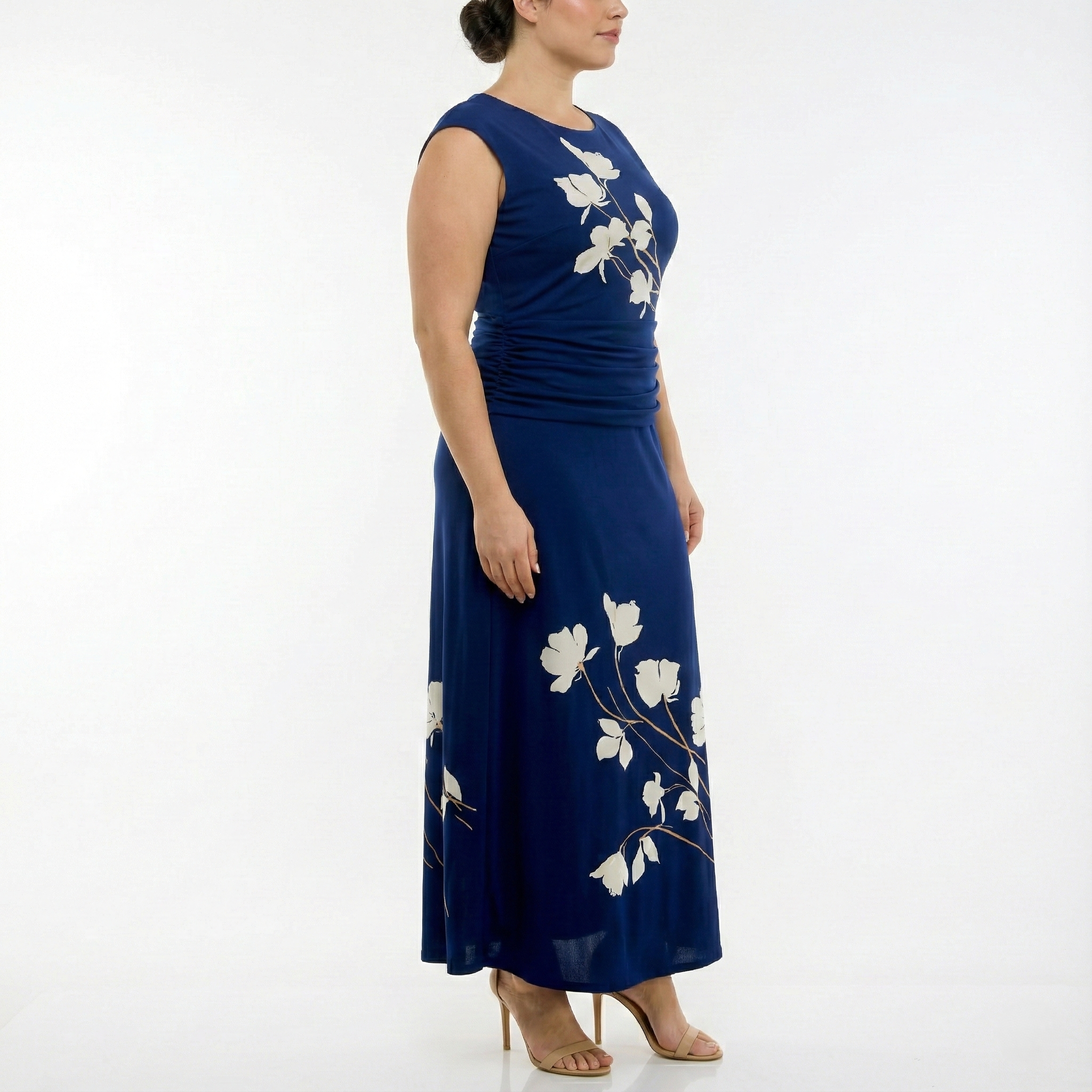 Side view of a women’s navy blue sleeveless maxi dress with ivory floral print, ruched waist, and flowing skirt, worn with nude heels.