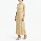 Side view of cornsilk yellow sleeveless midi dress featuring white floral pattern, fitted ruched bodice, flowing midi skirt, and nude high-heel sandals.