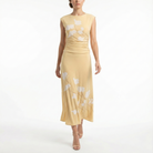 Model wearing a cornsilk yellow sleeveless midi dress with soft white floral print, ruched waist, and flowy skirt, styled with nude high-heel sandals.