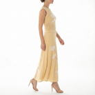 Side profile of model wearing a cornsilk yellow sleeveless midi dress with white floral print, ruched bodice, flowy midi skirt, and nude high-heel sandals.