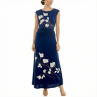 Front view of model wearing a navy sleeveless midi dress with ivory floral print, ruched waist, flowing skirt, and nude high-heel sandals.