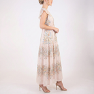 Side profile of blush pink floral chiffon maxi dress with flutter sleeves, smocked waist, lightweight sheer fabric, and tiered skirt, worn with nude heels.