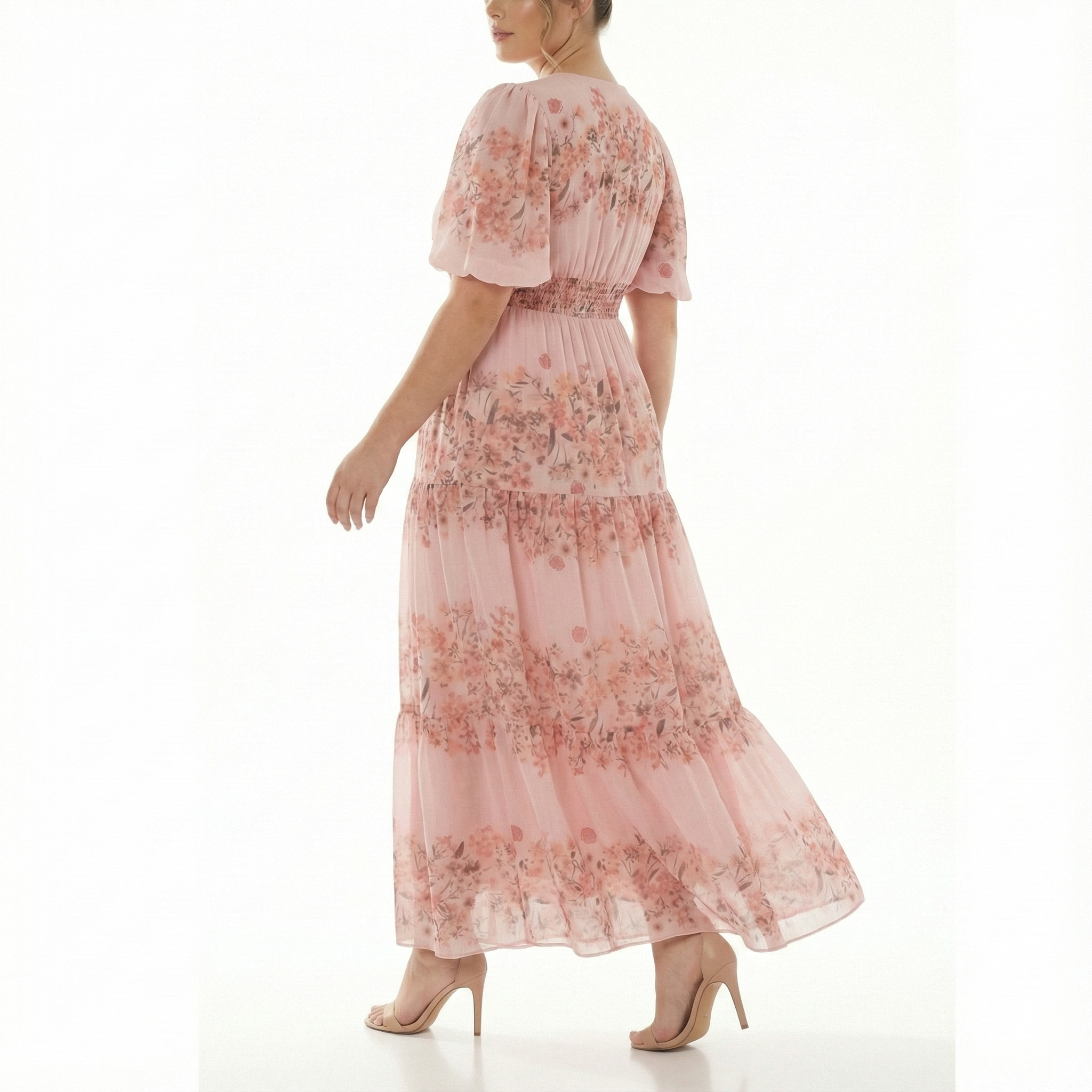Back three-quarter view of blush pink floral chiffon maxi dress with short puff sleeves, smocked waist, and flowing tiered skirt.