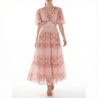 Blush pink floral chiffon maxi dress with short puff sleeves, V-neck twist bodice, fitted waist, and tiered skirt, shown from the front.