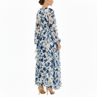 Back view of women’s blue and white floral chiffon maxi dress with long sheer sleeves, fitted empire waist, and flowing layered skirt.