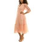 Three-quarter side view of a peach button-front midi dress with sheer fabric, elastic waistline, soft pleating, and tiered hem, styled with nude heels.