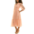 Side view of a peach chiffon midi dress highlighting the elastic waist, sheer sleeves, flowing skirt, and side pocket detail.
